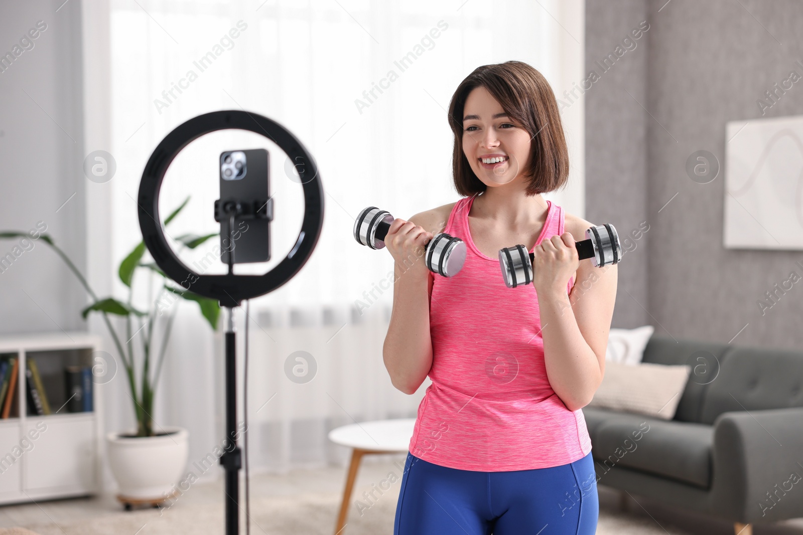 Photo of Happy sports blogger with dumbbells streaming online fitness lesson with smartphone at home