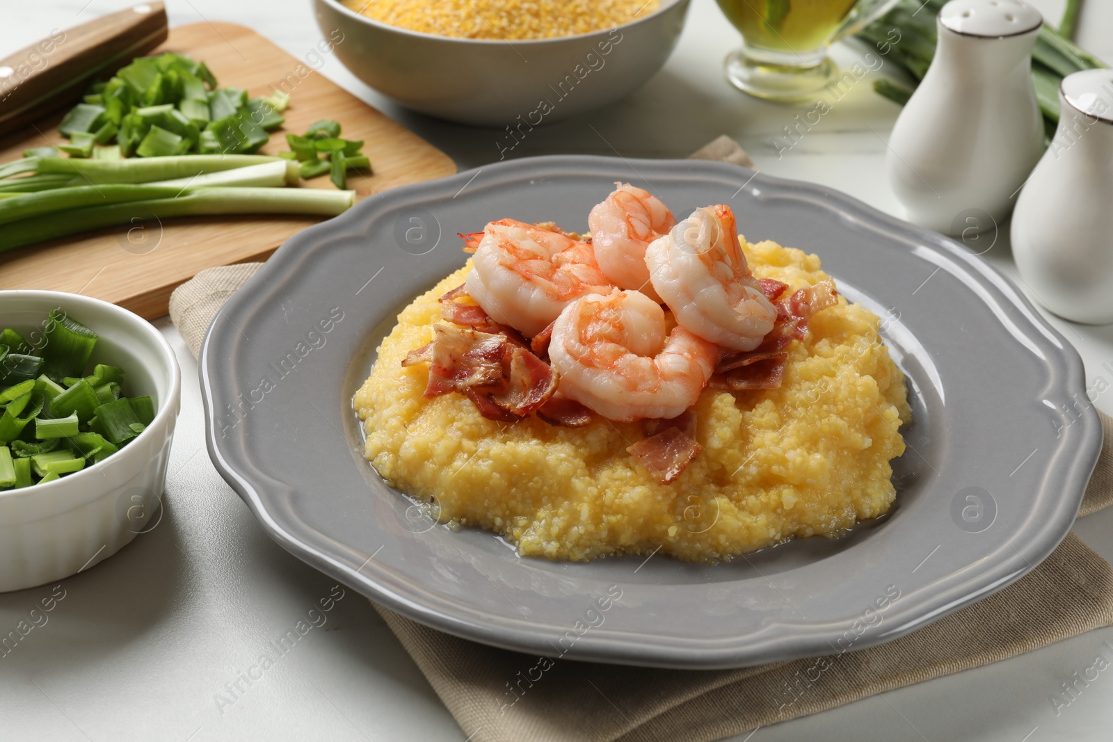 Photo of Plate with fresh tasty shrimps, bacon, grits and green onion on white marble table