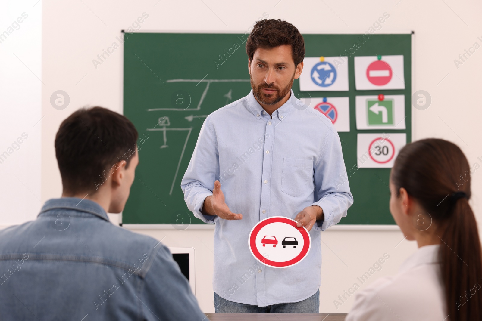 Photo of Teacher showing No Overtaking road sign during lesson in driving school