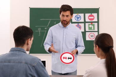 Teacher showing No Overtaking road sign during lesson in driving school