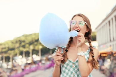 Photo of Young woman with cotton candy on city street. Space for text