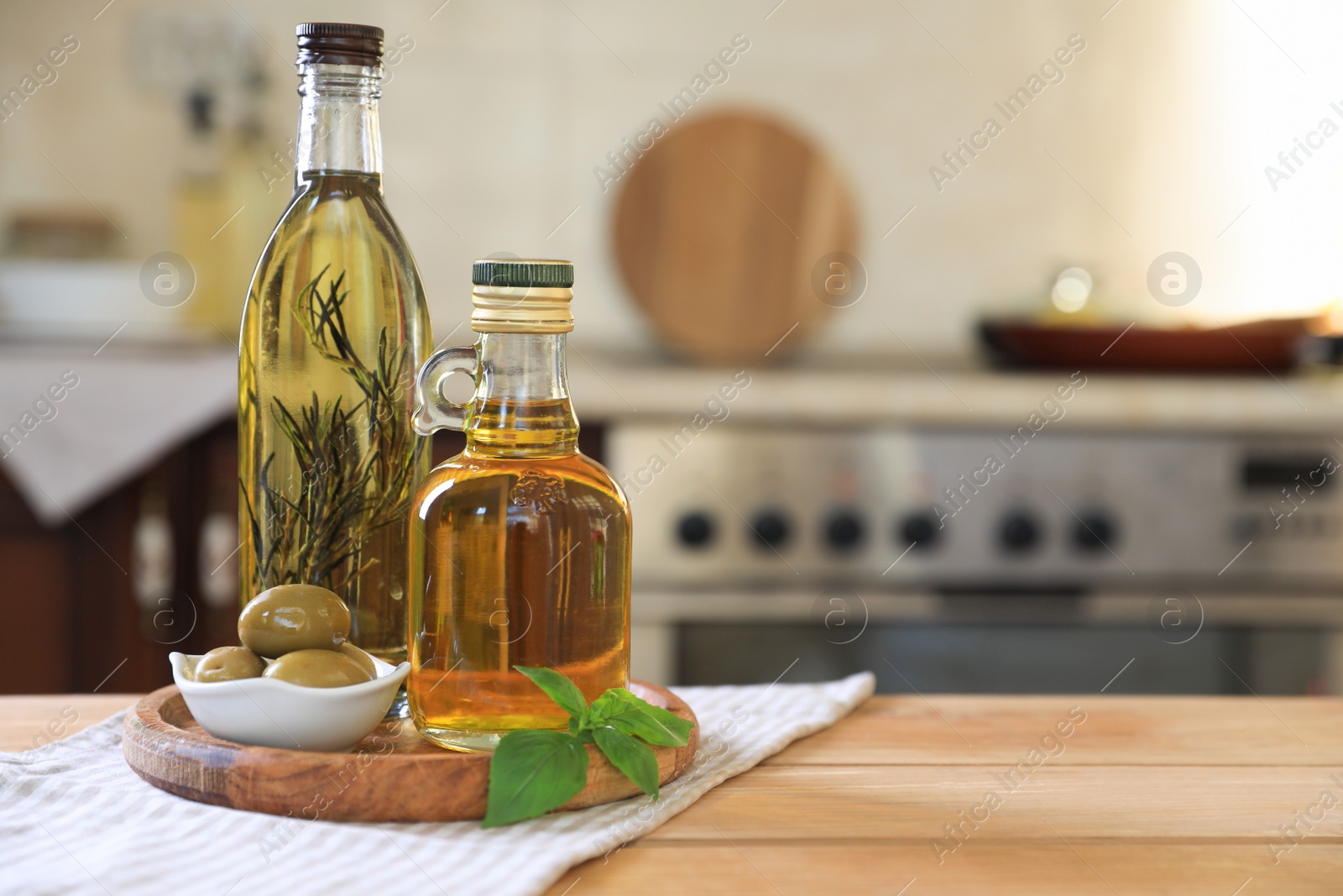 Photo of Different cooking oils, olives and basil on wooden table in kitchen, space for text