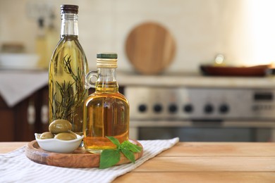Different cooking oils, olives and basil on wooden table in kitchen, space for text
