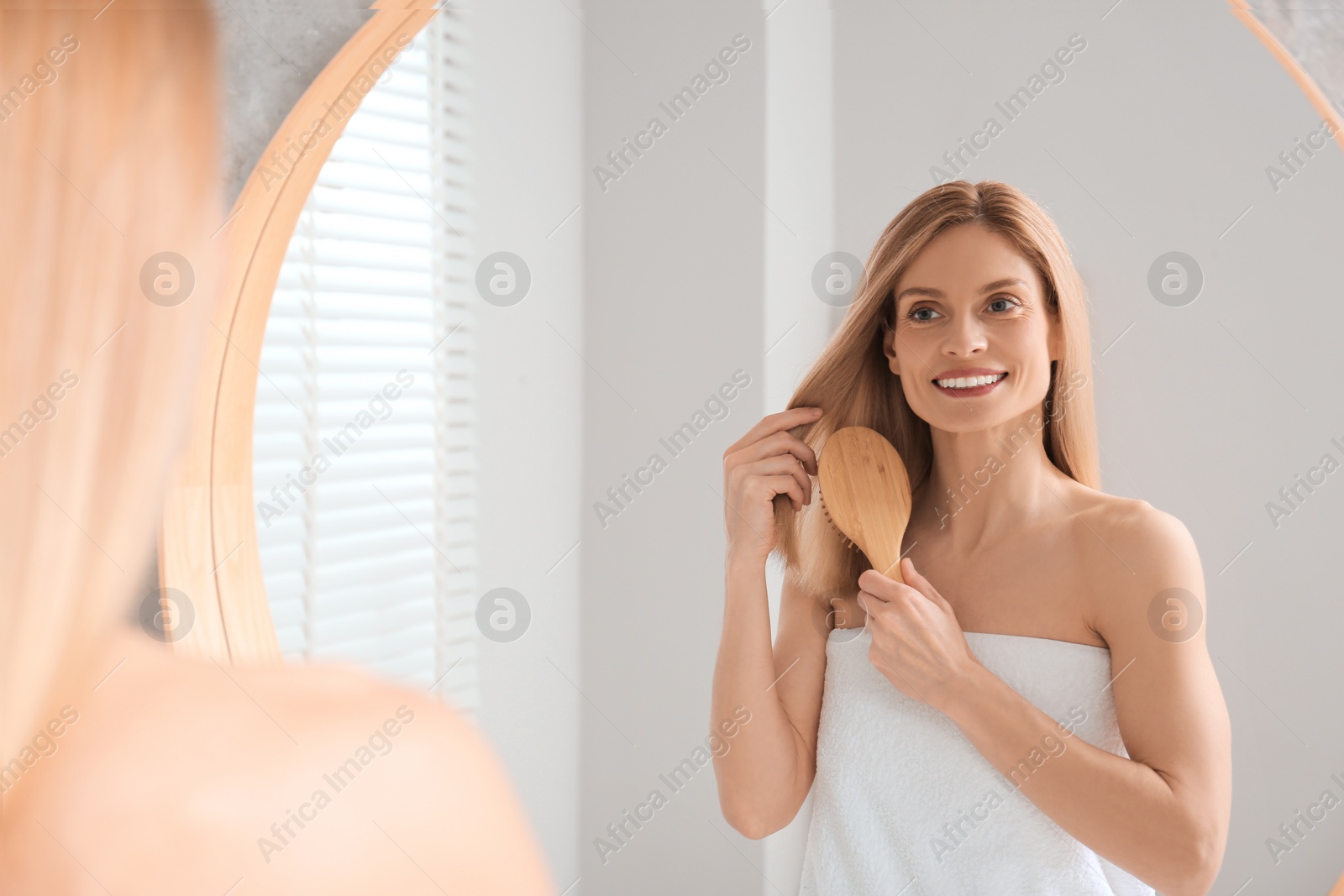 Photo of Beautiful woman brushing her hair near mirror in bathroom