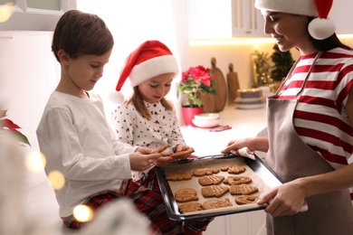 Mother giving her cute little children freshly baked Christmas cookies in kitchen
