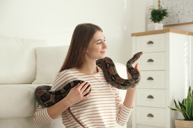 Photo of Young woman with boa constrictor at home. Exotic pet