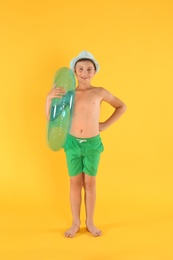 Photo of Cute little child in beachwear with bright inflatable ring on yellow background