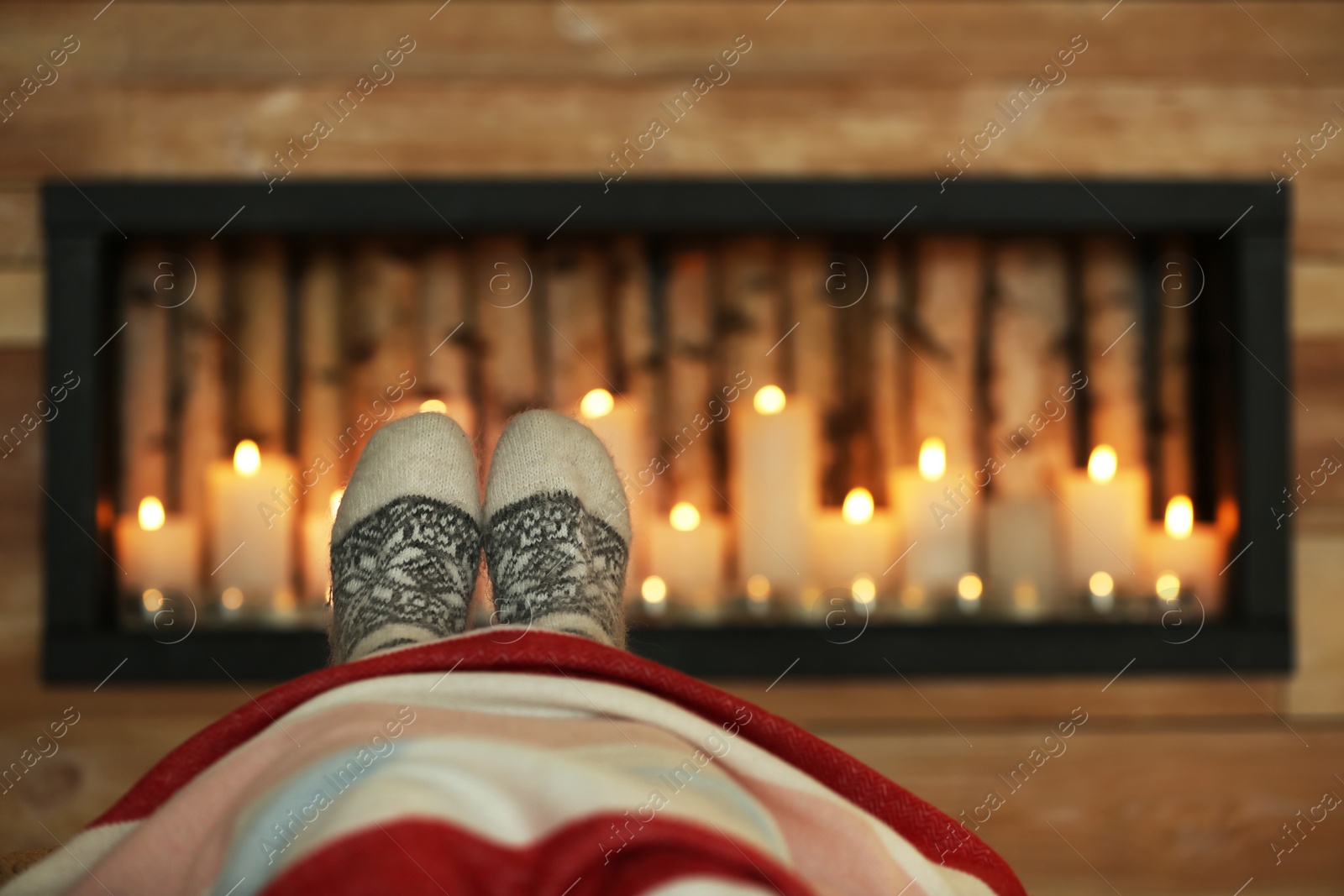 Photo of Woman wearing warm knitted socks near decorative fireplace indoors, closeup. Winter atmosphere