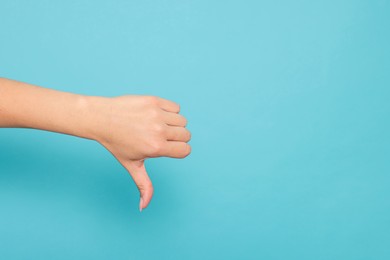 Woman showing thumb down on light blue background, closeup. Space for text