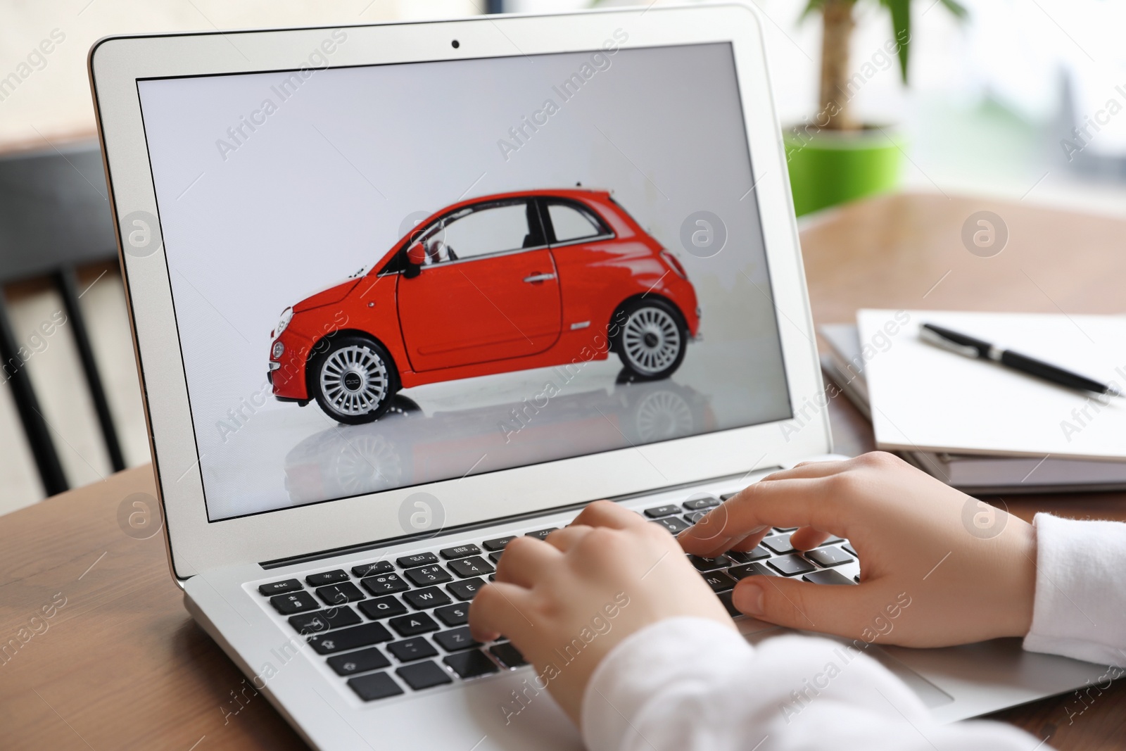 Photo of Woman using laptop to buy car at wooden table indoors, closeup