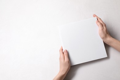 Photo of Woman holding book with blank cover at white table, top view. Mockup for design