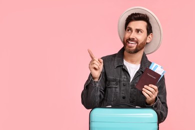 Photo of Smiling man with passport, tickets and suitcase pointing at something on pink background. Space for text