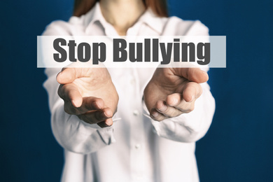 Young woman showing sign STOP BULLYING on blue background, closeup 