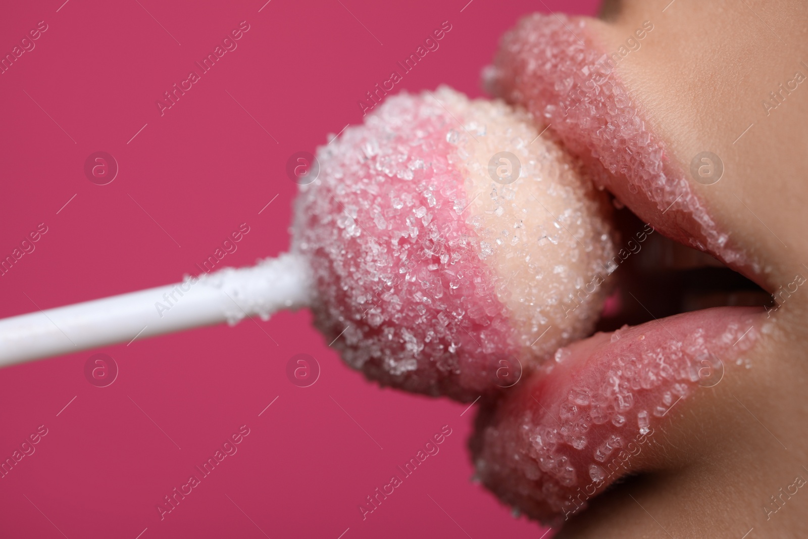 Photo of Young woman with beautiful lips covered in sugar eating lollipop on pink background, closeup