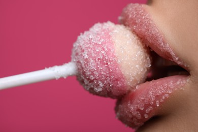 Photo of Young woman with beautiful lips covered in sugar eating lollipop on pink background, closeup