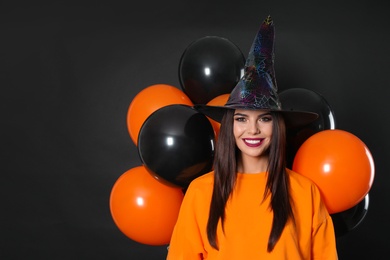 Photo of Beautiful woman wearing witch costume with balloons for Halloween party on black background