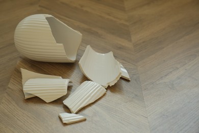 Photo of Broken white ceramic vase on wooden floor. Space for text