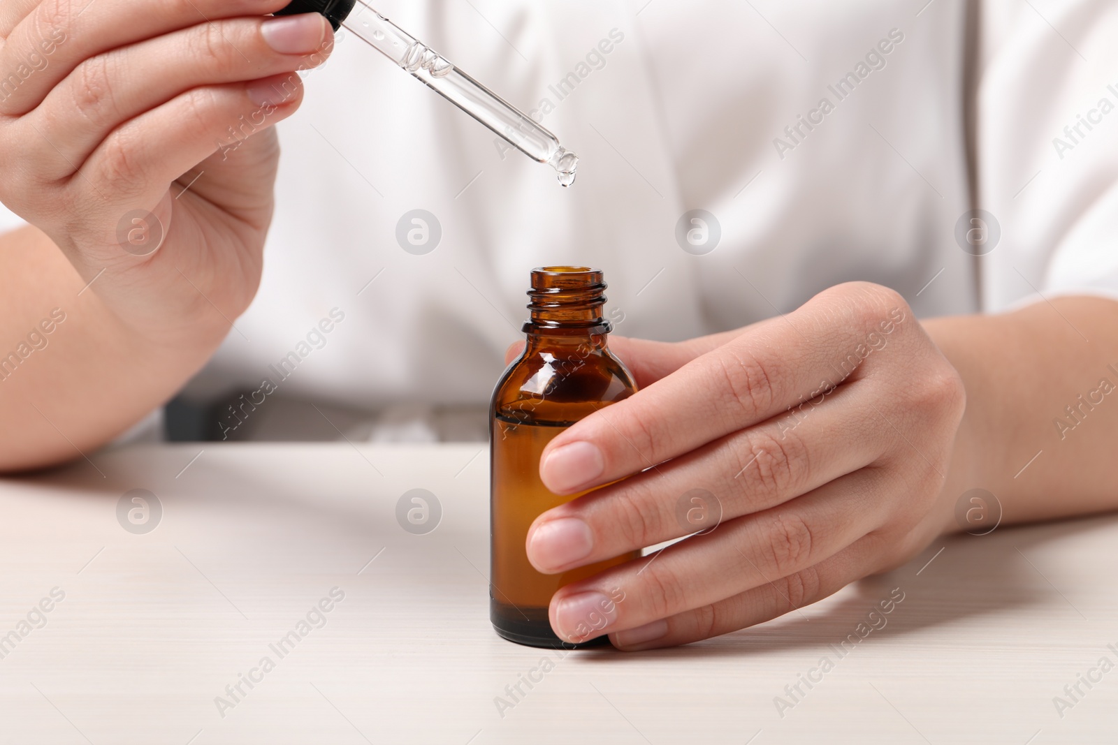 Photo of Woman with bottle of cosmetic serum and pipette at white table, closeup