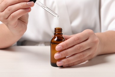 Woman with bottle of cosmetic serum and pipette at white table, closeup