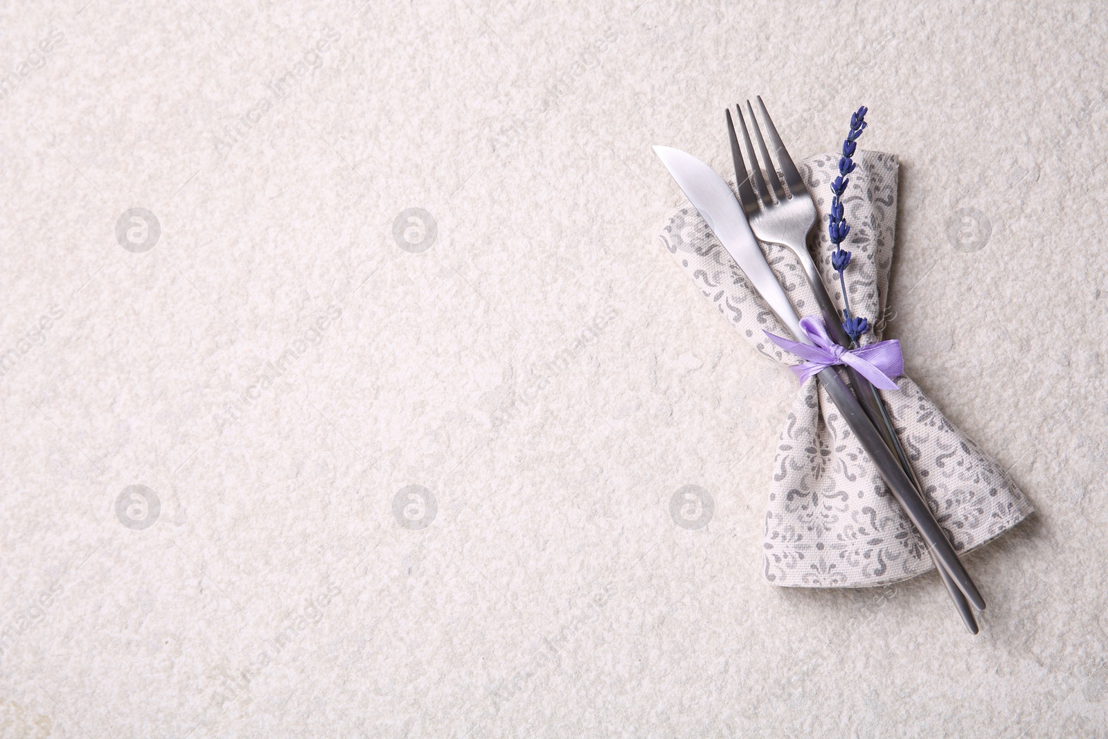 Photo of Cutlery, napkin and preserved lavender flower on white textured table, top view. Space for text