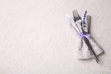 Cutlery, napkin and preserved lavender flower on white textured table, top view. Space for text