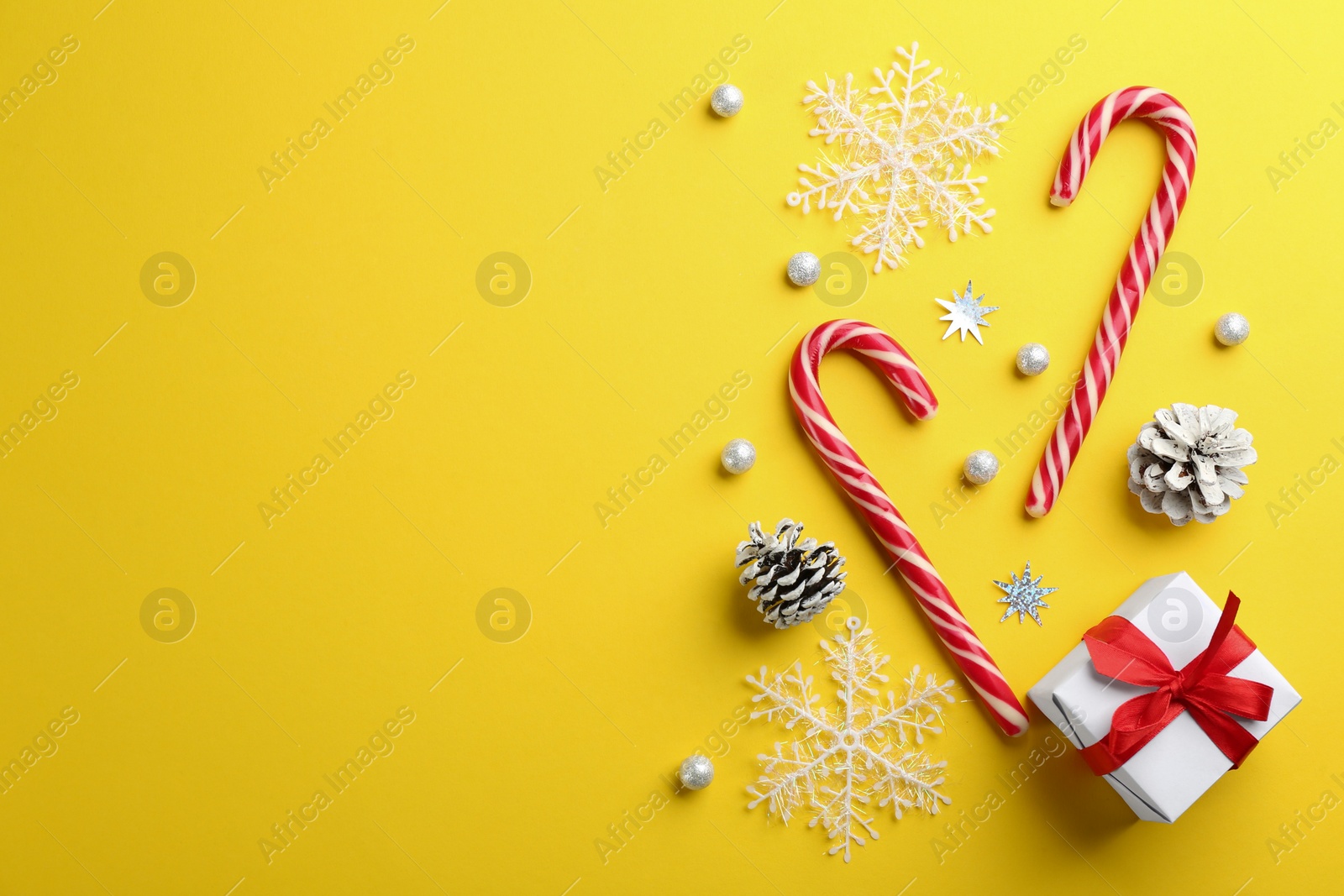 Photo of Flat lay composition with candy canes and Christmas decor on yellow background. Space for text