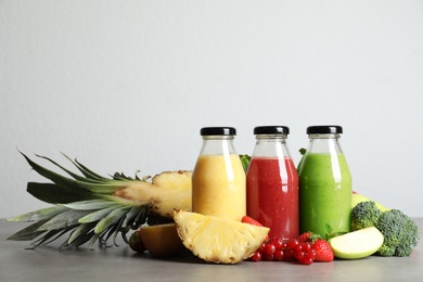 Bottles of delicious juices and fresh fruits on grey table