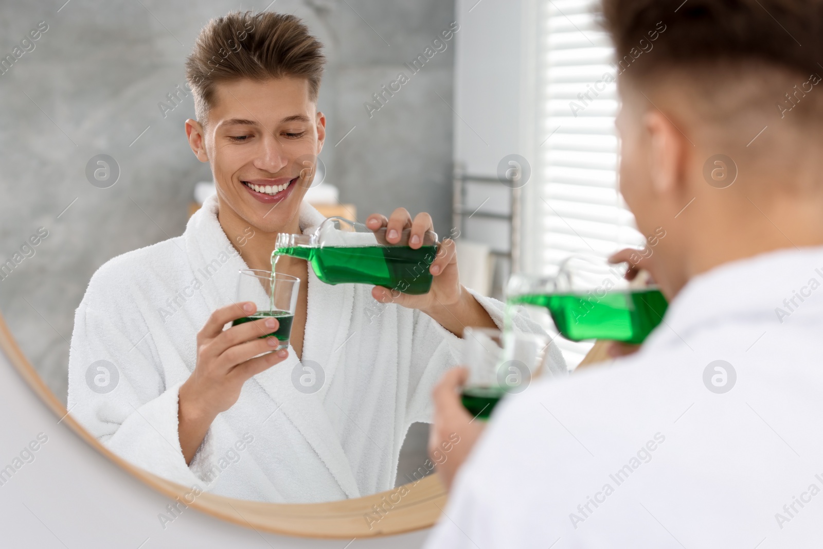 Photo of Young man using mouthwash near mirror in bathroom