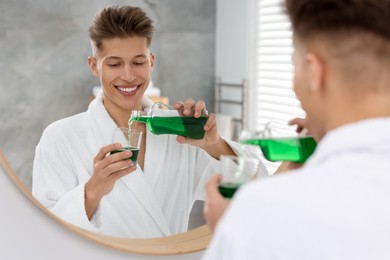 Young man using mouthwash near mirror in bathroom