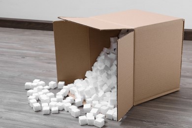 Photo of Overturned cardboard box with styrofoam cubes on wooden floor indoors