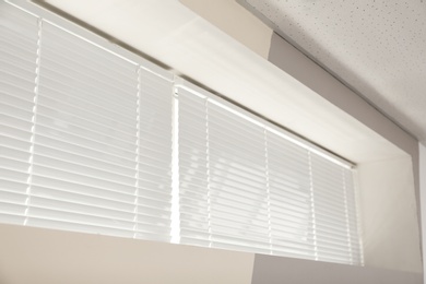 Photo of Modern window with closed white blinds indoors