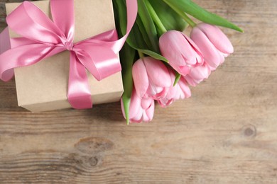 Photo of Gift box and beautiful tulip flowers on wooden table, flat lay. Space for text