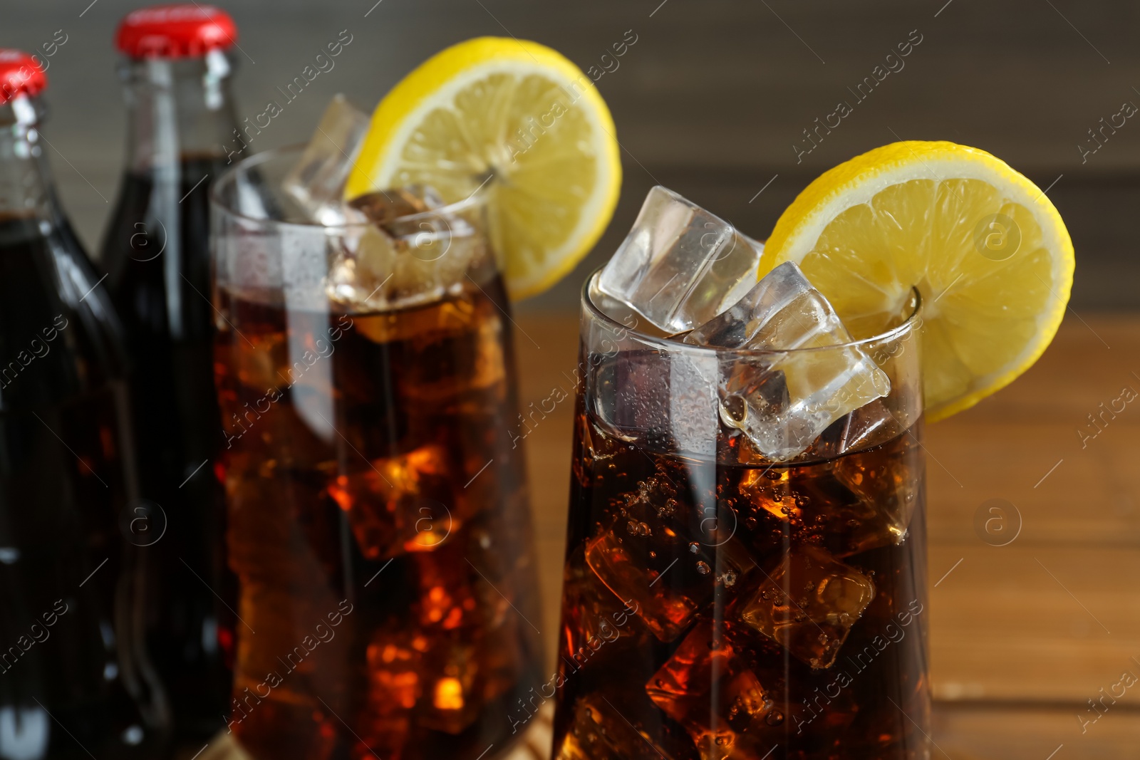 Photo of Glasses of refreshing soda water with ice and lemon slices on blurred background, closeup