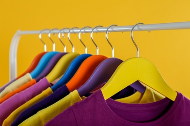 Rack with stylish children clothes on yellow background, closeup