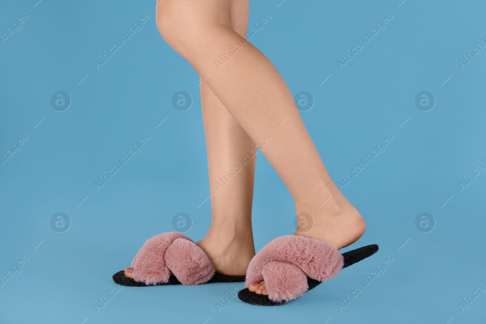 Photo of Woman in fluffy slippers on light blue background, closeup