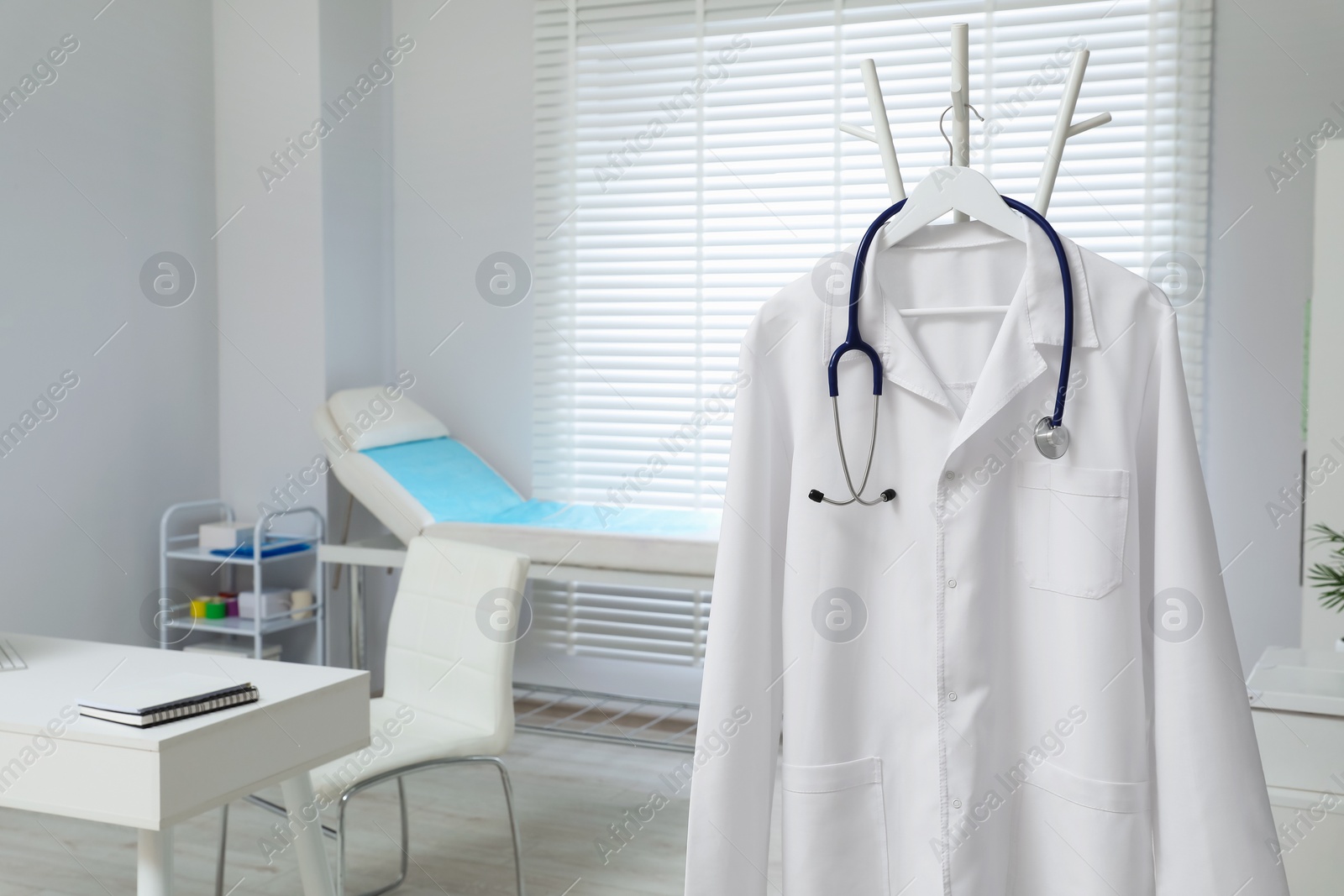 Photo of White doctor's gown and stethoscope hanging on rack in clinic. Space for text