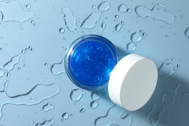 Open jar of cosmetic product and water drops on light blue background, top view