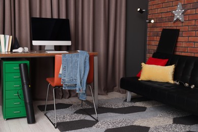 Photo of Stylish teenager's room with computer and black sofa near brick wall