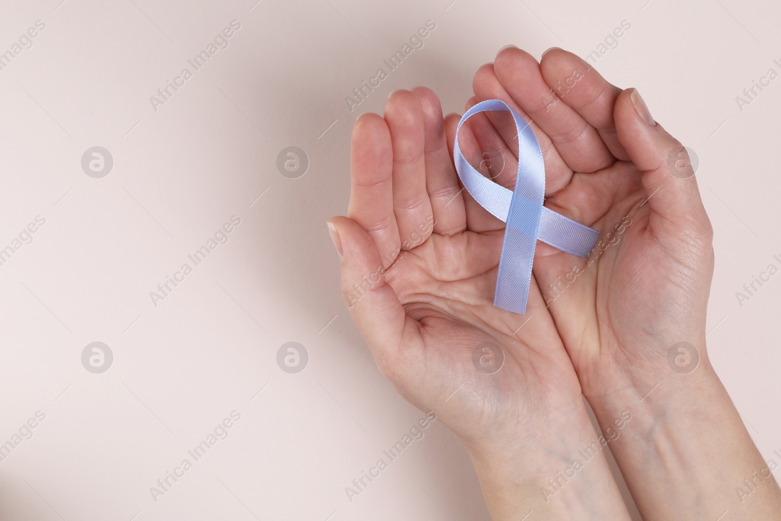 Photo of International Psoriasis Day. Woman with light blue ribbon as symbol of support on beige background, top view. Space for text