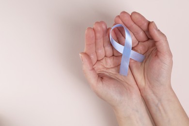 Photo of International Psoriasis Day. Woman with light blue ribbon as symbol of support on beige background, top view. Space for text