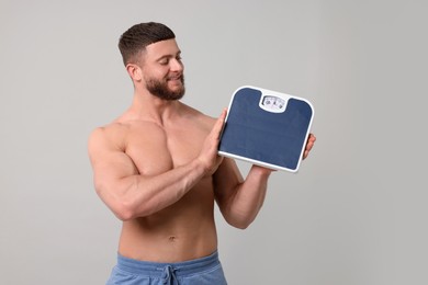 Photo of Happy athletic man holding scales on light grey background. Weight loss concept