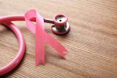 Photo of Pink ribbon and stethoscope on wooden background, space for text. Breast cancer concept