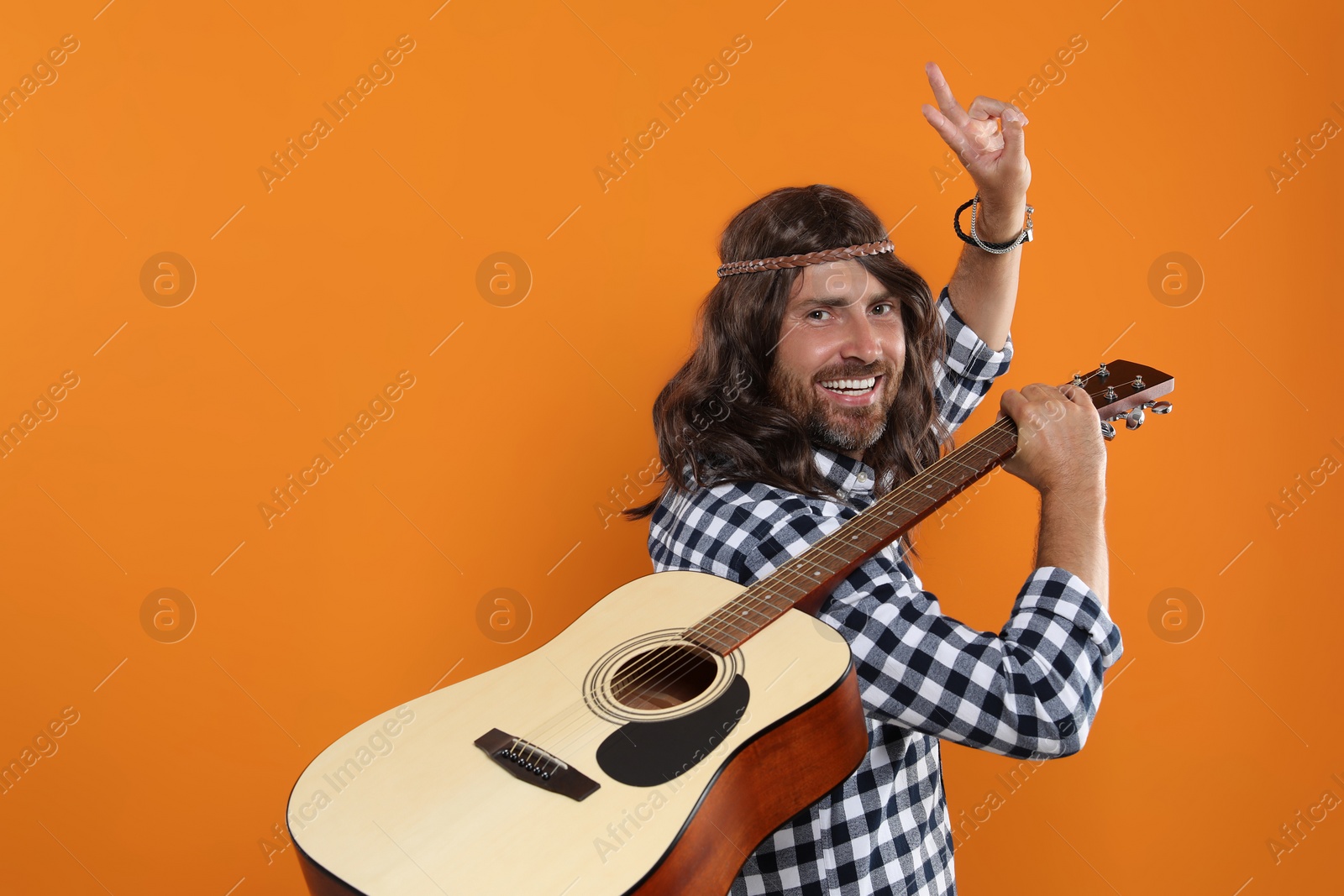 Photo of Hippie man with guitar showing V-sign on orange background, space for text