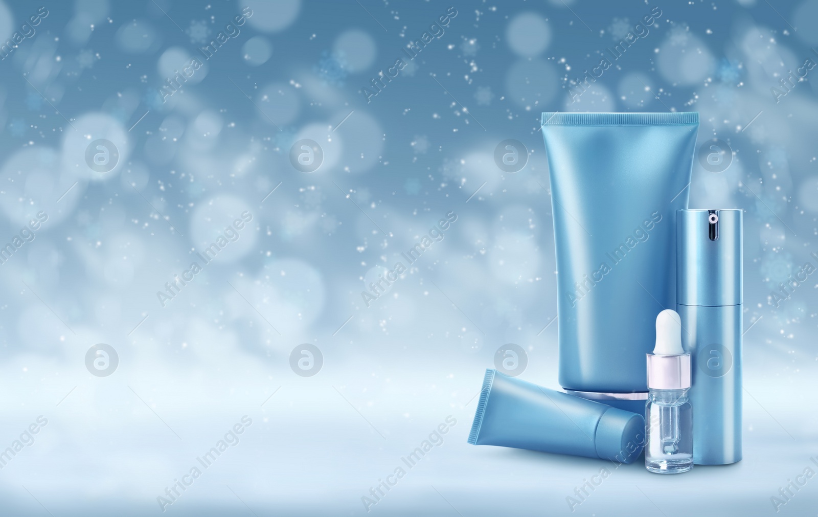 Image of Different cosmetic products on blue background with blurred snowflakes, space for text. Winter skin care