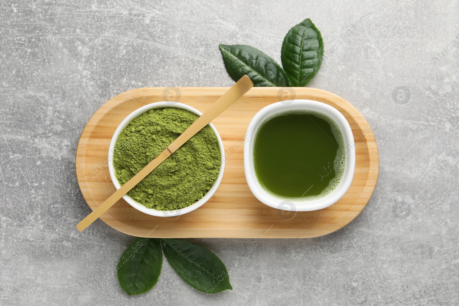 Photo of Green matcha powder, bamboo scoop, fresh beverage and leaves on light grey table, flat lay