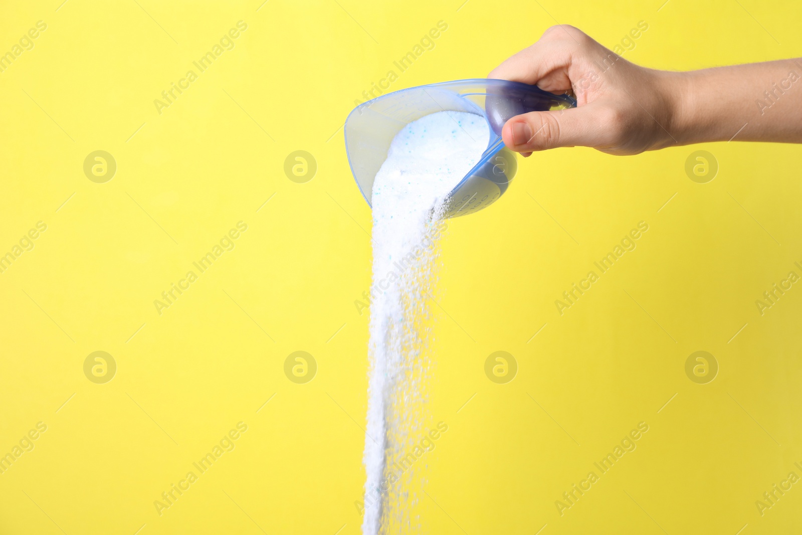 Photo of Woman pouring laundry powder from measuring cup on yellow background, closeup