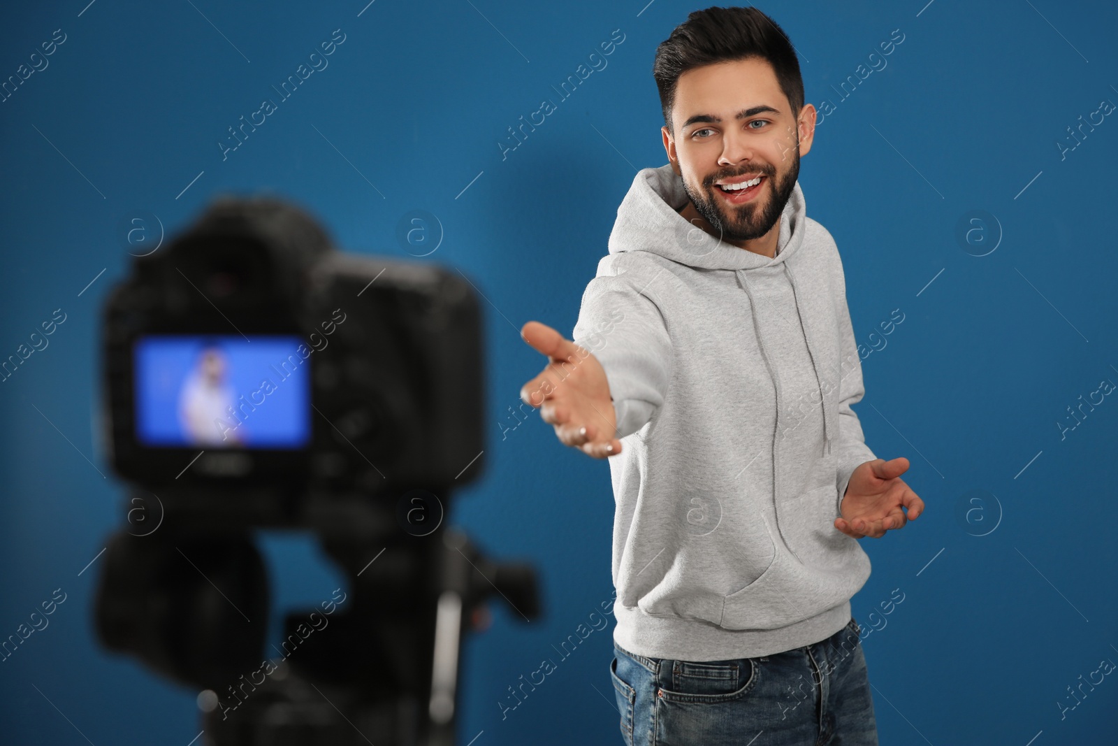 Photo of Young blogger recording video on camera against blue background