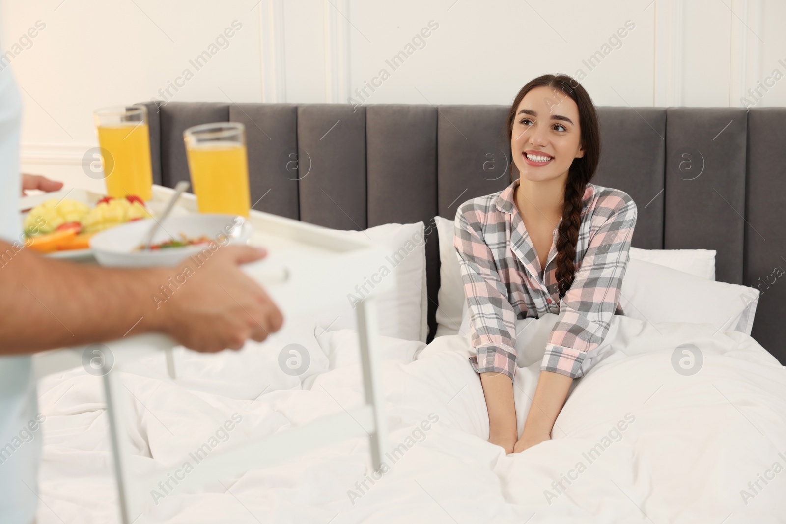 Photo of Man bringing white tray with breakfast to happy young woman on bed at home