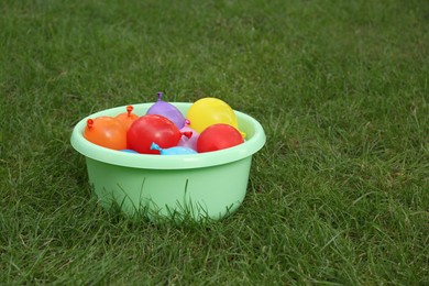 Basin full of water bombs on green grass. Space for text