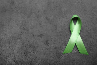 Photo of World Mental Health Day. Green ribbon on black background, top view with space for text